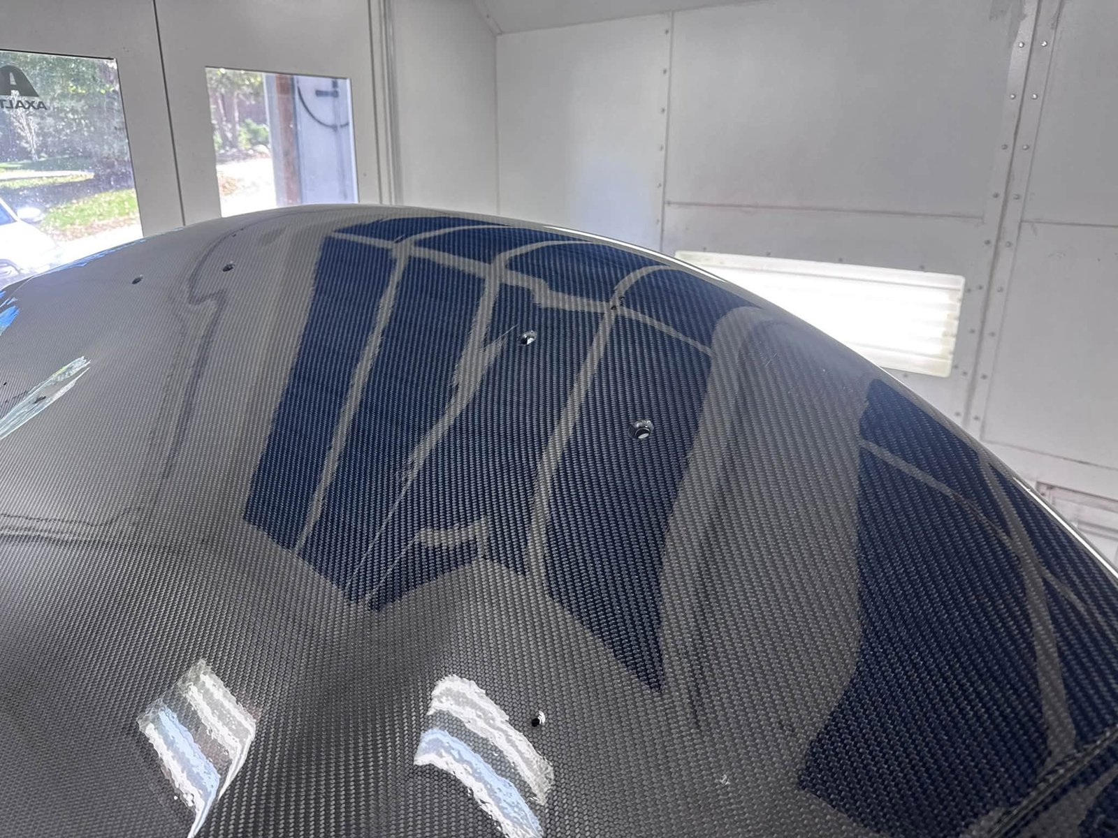 Glossy carbon-fiber panel reflecting paint booth lights